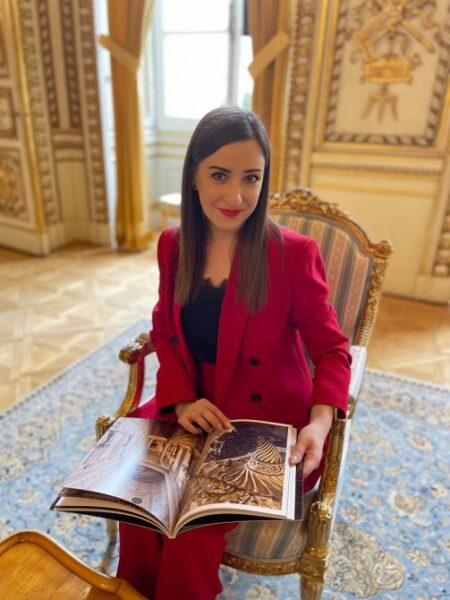 Dr Zoriana Czajkowska siedzi na fotelu z albumem fotograficznym na kolanach. Siedzi w eleganckim pomieszczeniu