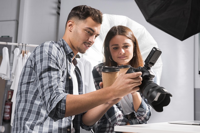 młody mężczyzna tłumaczy funkcje aparatu fotograficznego dziewczynie, która stoi koło niego