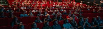 Pełna sala kinowa z ludźmi wpatrującymi w ekran