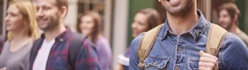 młody mężczyzna student stoi z plecakiem i książkami w ręku i się uśmiecha