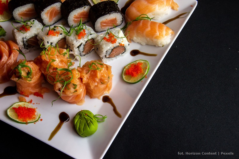 Potrawa sushi ozdobnie ułożona na widzianym częściowo w kadrze talerzu kwadratowym