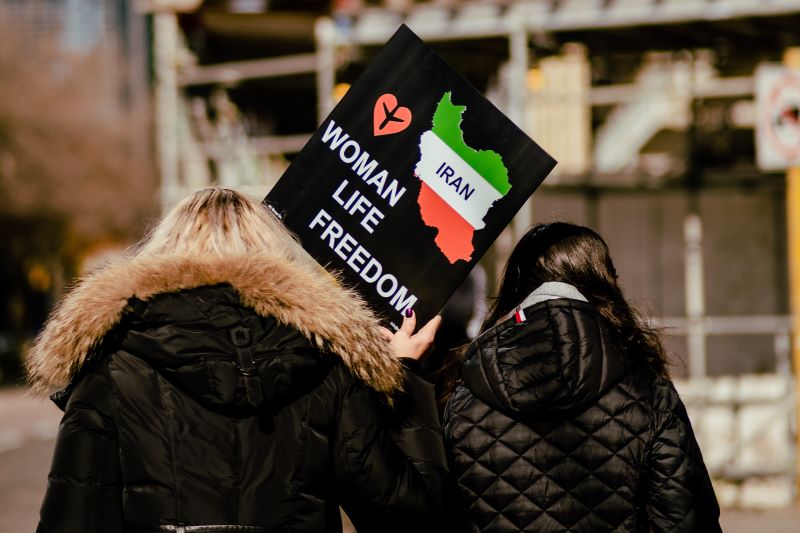 Dwie kobiety widziane od tyłu z transparentem nawołującym o wolność kobiet w Iranie