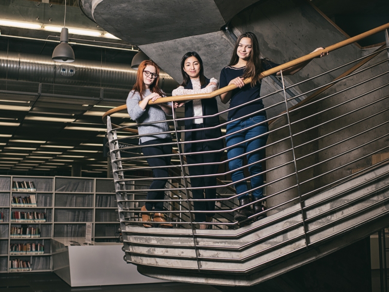 Trzy młode kobiety stojące na schodach w bibliotece