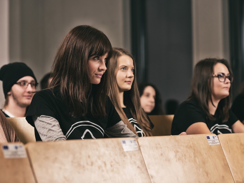 Grupa młodych ludzi słuchających wykładu w sali sympozjalnej