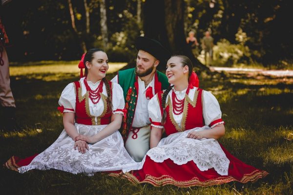 Członkowie Studenckiego Zespołu Pieśni i Tańca „Katowice” ubrani w tradycyjne stroje siedzą na trawie