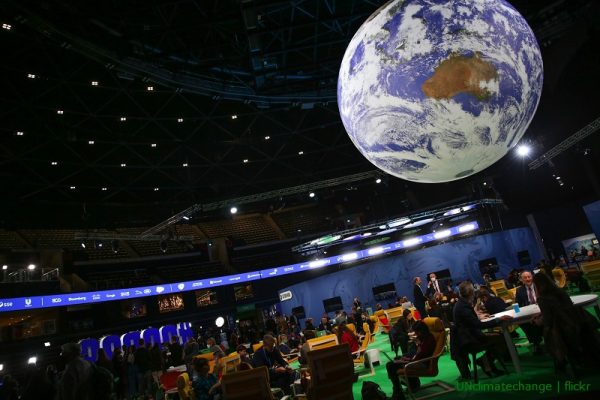 Widok na podwieszoną kulę ziemską w przyciemnionej sali konferencyjnej pełnej ludzi siedzących przy stolikach