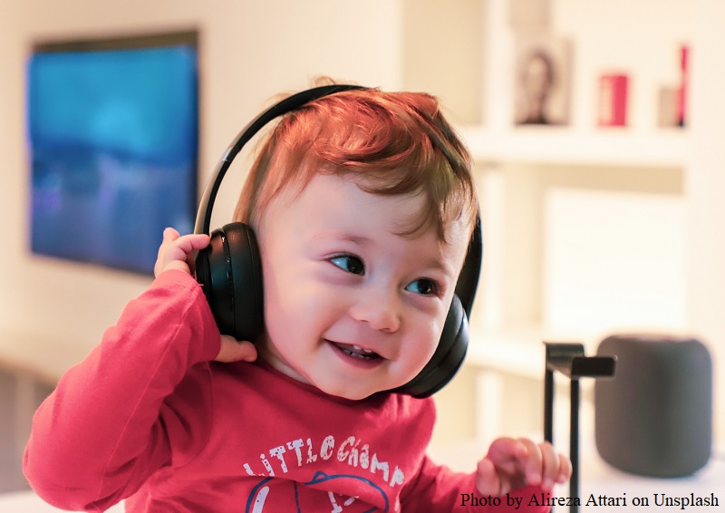 Uśmiechnięte małe dziecko ma założone na uszy czarne słuchawki