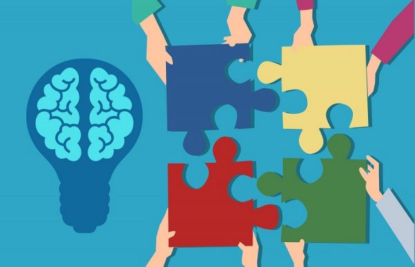 grafika przedstawiająca dłonie czterech osób trzymających puzzle, obok żarówka z rysunkiem mózgu/graphic showing the hands of four people holding puzzles next to a lightbulb with a picture of the brain