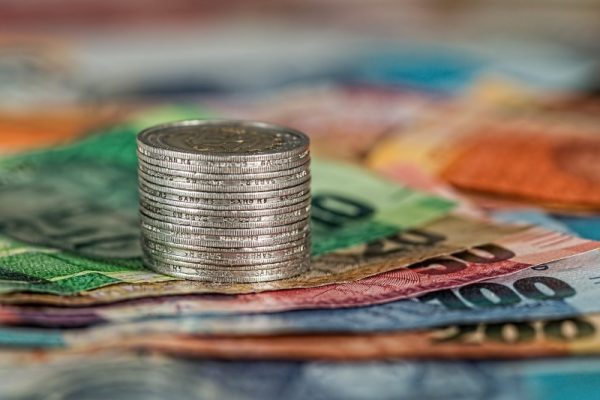 Kolorowe leżące banknoty o różnych nominałach. Na nich stoi stosik kilkunastu srebrnych monet