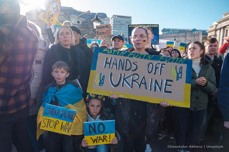 Stłoczeni ludzie z transparentami i owinięci ukraińskimi flagami głoszą wsparcie dla Ukrainy