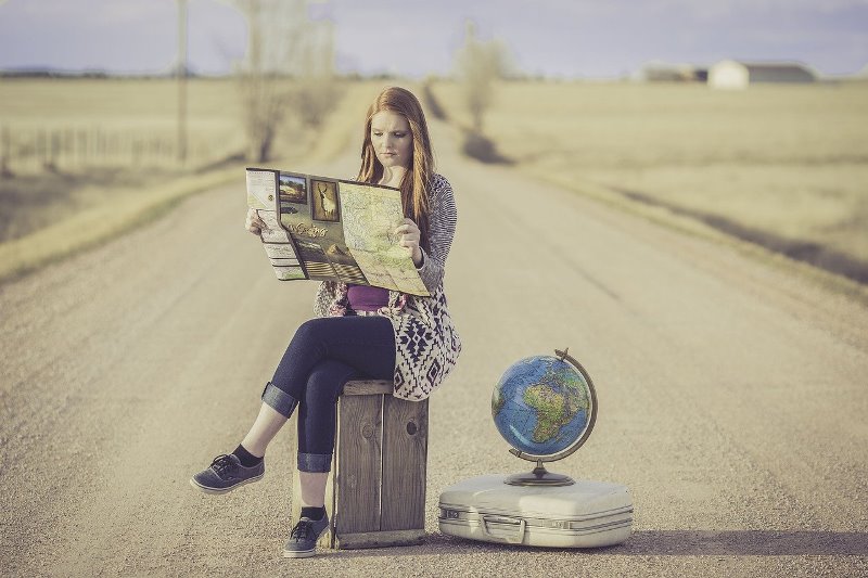 Dziewczyna z mapą siedząca na walizce, obok druga walizka i globus