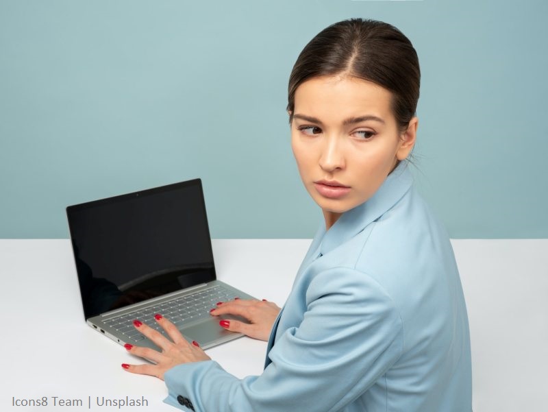 Kobieta siedząca przy laptopie, spoglądająca przez ramię
