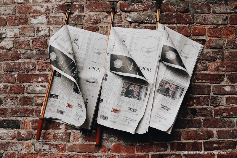 Szpalty trzech gazet wiszące na ceglanym murze/Three newspapers hanging on a brick wall