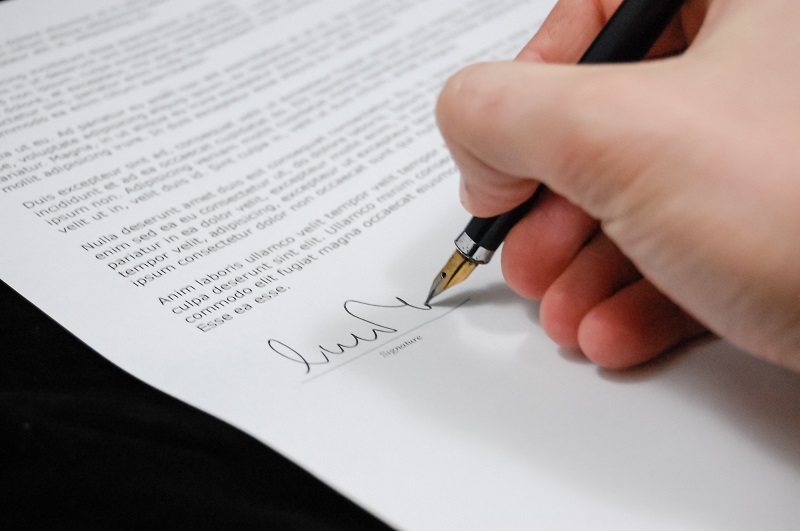 Dłoń trzymająca długopis i podpisująca dokument