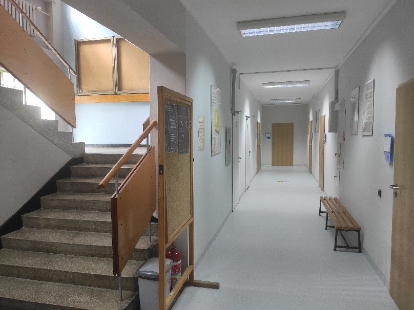 po lewej klatka schodowa, schody w górę. Po prawej korytarz, drzwi do pomieszczeń i ławka./On the left a staircase, stairs leading upstairs. On the right a corridor, doors to rooms and a bench.