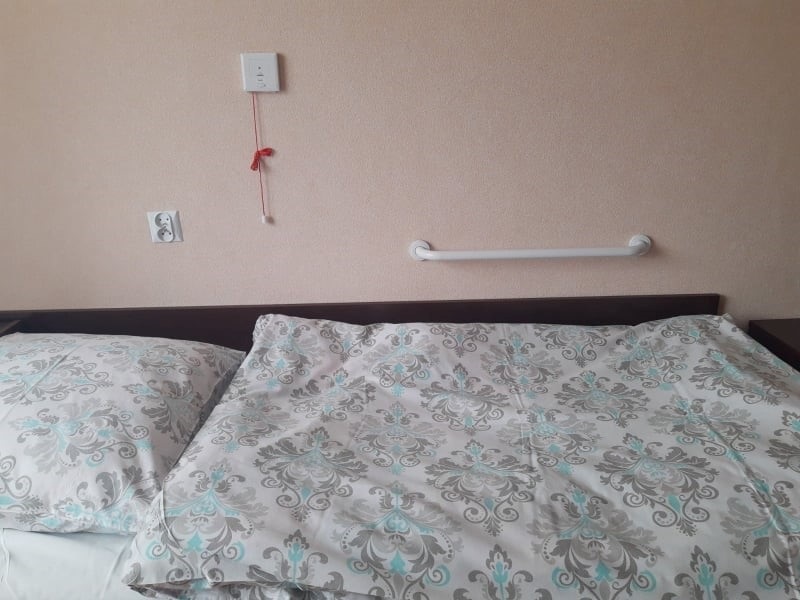 Zbliżenie na łóżko z uchwytem i przyciskiem alarmowym./Close-up of a bed with a holder and alarm button.