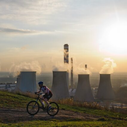 rowerzysta wjeżdżający pod górę, w tle kominy elektrowni