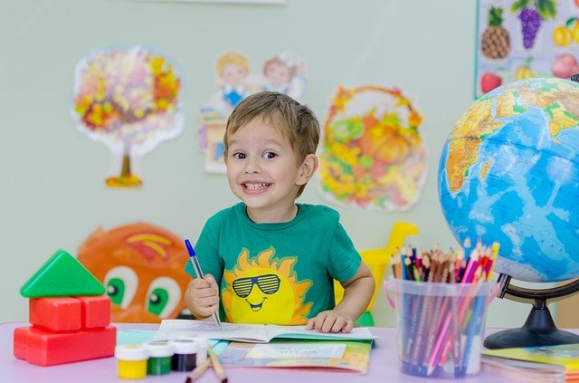 kolorowe zdjęcie: mały cuśmiechnięty chłopiec z globusem i mnóstwem kolorowych kredek