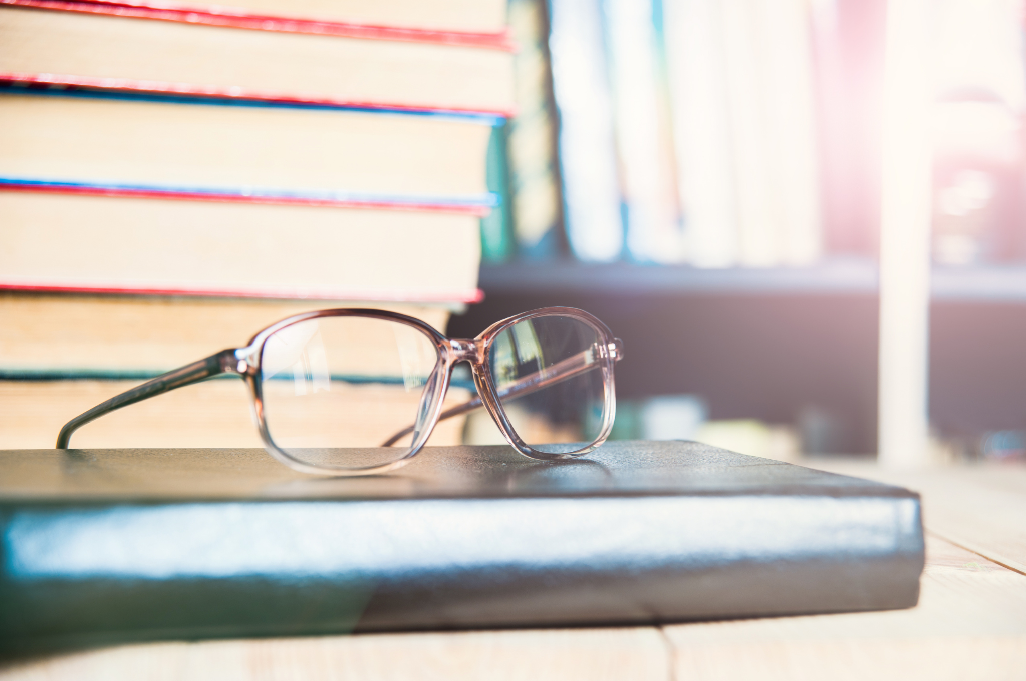 okulary leżące na książce, w tle sterta książek