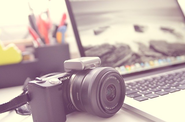 aparat fotograficzny i otwarty laptop leżące na biurku