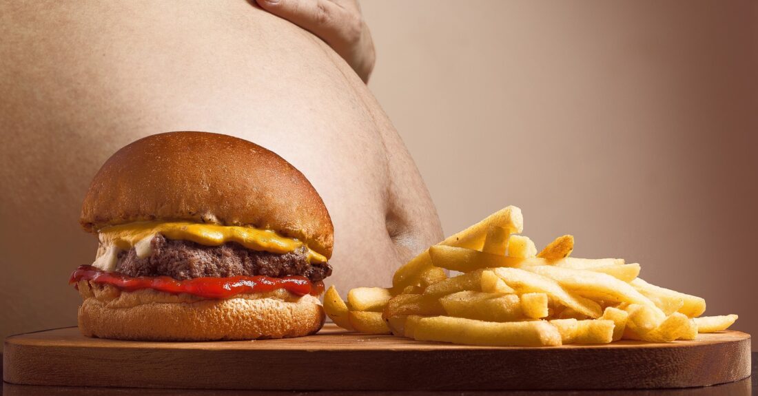 hamburger i frytki, w tle duży brzuch