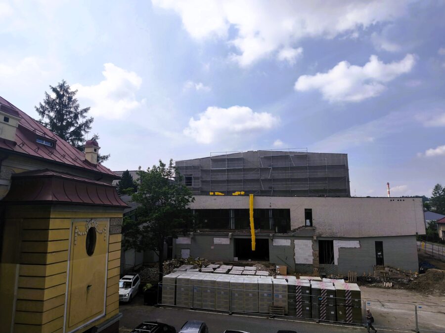 Fot.2 Widok na budynek w trakcie przebudowy z rusztowaniami na górnej kondygnacji oraz materiałami budowlanymi składowanymi przed wejściem. Na pierwszym planie widoczny jest fragment zabytkowego budynku Wydziału Sztuki i Nauk o Edukacji z jasną elewacją i czerwonym dachem.